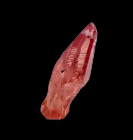 A close-up image of The Crystalary's Rhodochrosite from the Uchucchacua Mine near Lima, Peru, showcases a vibrant red crystal with a rough, jagged texture. Set against a solid black background, the well-defined crystal reveals its intricate surface details and stunning coloration.