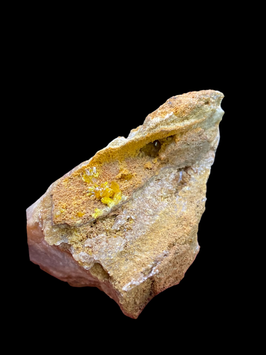 A striking piece of Legrandite from The Crystalary, sourced from the famous Ojuela Mine in Mapimí, Mapimí Municipality, Durango, Mexico, is nestled in a tan-colored matrix rock and showcased against a black background. The Legrandite exhibits a crystalline structure with several small, shiny facets gleaming on its surface.