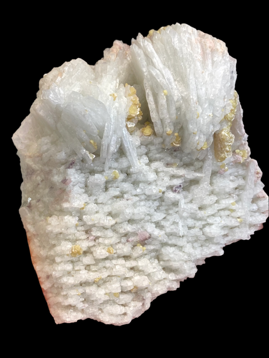 Presenting the Cookeite, Lepidolite, Albite specimen from The Crystalary, sourced from Itinga, Bahia, Brazil. This captivating white mineral features fibrous, needle-like crystal formations at the top and a granular, rough texture at the base. Interspersed throughout are small yellowish inclusions of cookeite. The striking black background accentuates its natural beauty.