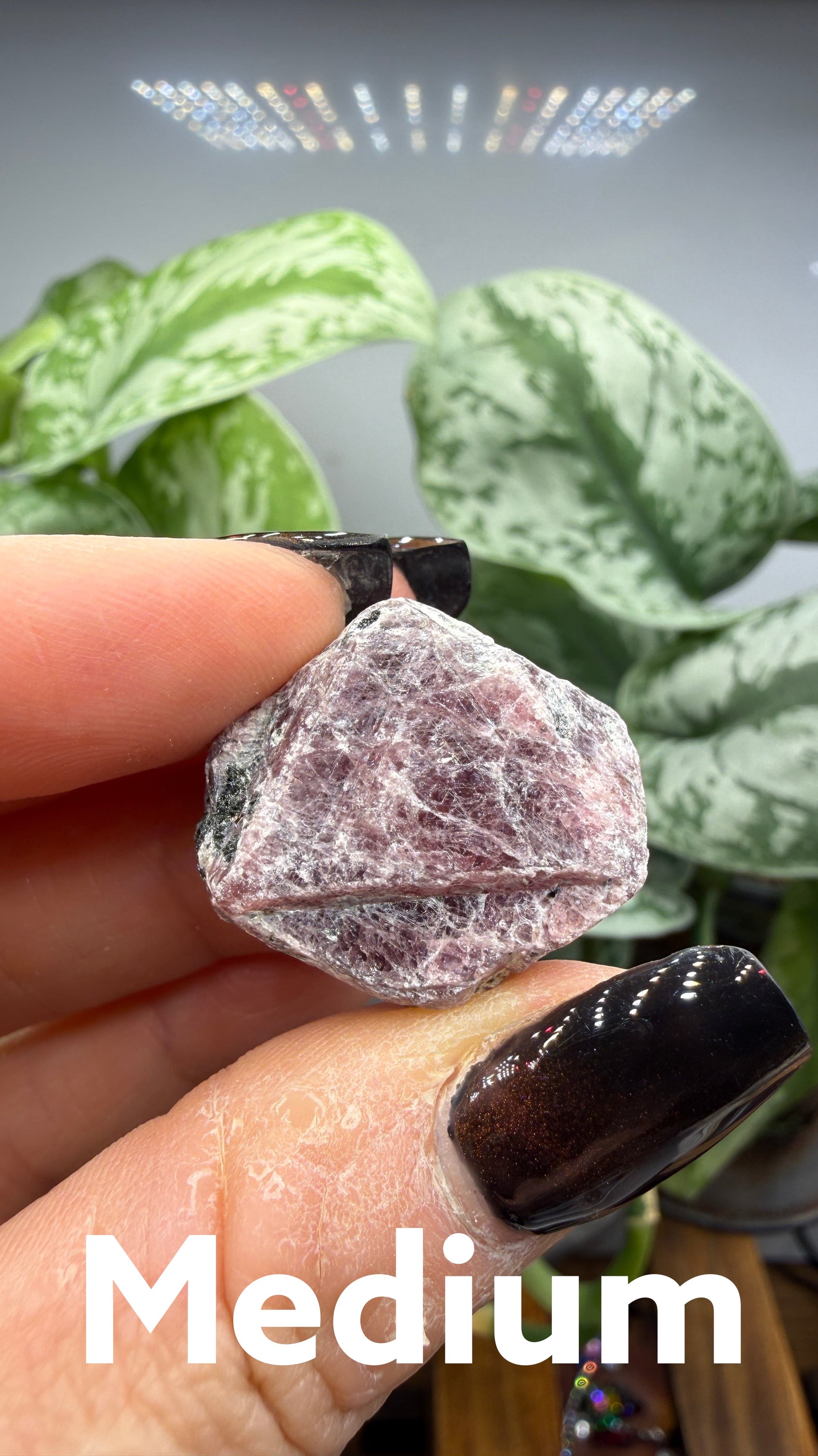 The Crystalary rough hexagonal corundum crystal in dusty rose and mauve tones held between fingers