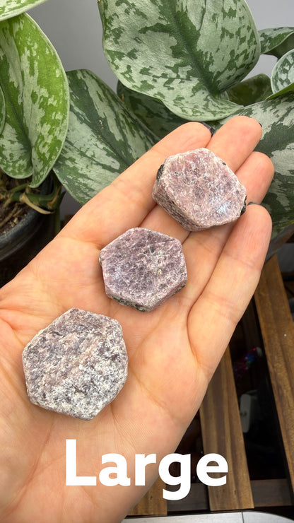 The Crystalary rough hexagonal corundum crystals in shades of dusty rose and mauve held in a person's palm.